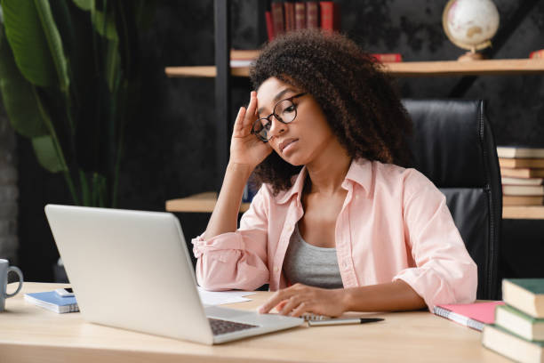 agotado cansado triste deprimido enfermo exceso de trabajo joven africana tutora estudiante independiente que tiene problemas en el trabajo, sufre de dolor de cabeza, migraña en la oficina del lugar de trabajo. - financial burden fotografías e imágenes de stock