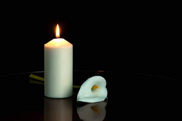 WHITE CALLA FLOWER NEXT TO A LIGHTED CANDLE ON DARK BACKGROUND. COPY SPACE. WHITE CALLA FLOWER NEXT TO A LIGHTED CANDLE ON DARK BACKGROUND. COPY SPACE. place of burial photos stock pictures, royalty-free photos & images