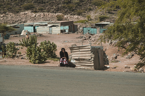 Djibouti, Djibouti - May 21, 2021: A Djiboutian woman sitting by the roadside under the sun. Editorial shot in Djibouti
