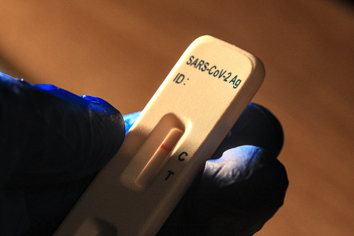 It's a hand wearing a blue glove and holding a negative covid 19 (sars-cov-2) self-test in the hand.