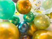 Close up of latex shiny balloons for party celebration – clear balloon with gold confetti inside, teal, purple, green, blue, white, green and gold balloons all tight together