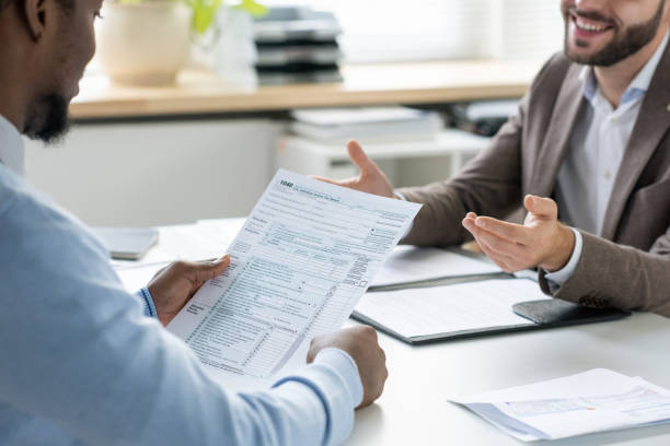 Hands of young lawyer talking to African male client looking through financial document Hands of young lawyer talking to African male client looking through financial document during consultation tax plan discution stock pictures, royalty-free photos  images