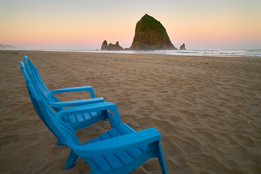 Beach chairs at sunrise with a view of Haystack Rock. Cannon Beach, Oregon, United States.