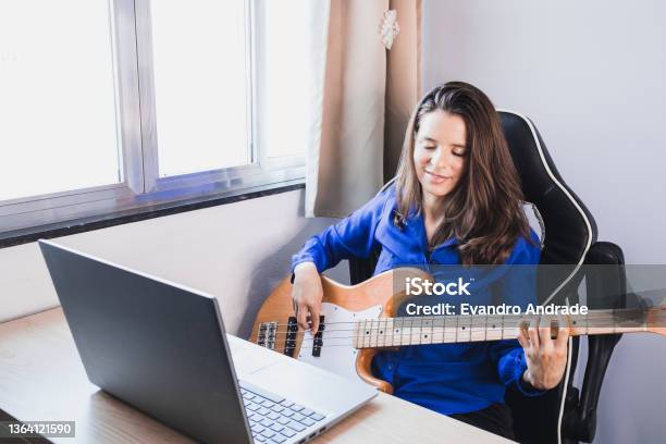 Woman Studying Music Online In Note Book And Playing Electric Bass Guitar Stock Photo - Download Image Now