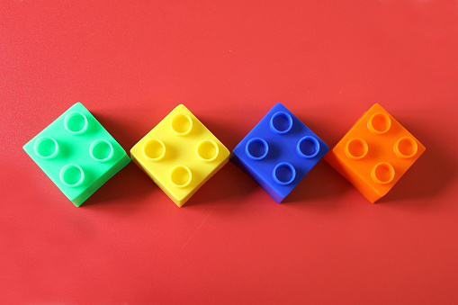 Buildable colored plastic blocks to play, build and organize on a red background as a concept of inclusion