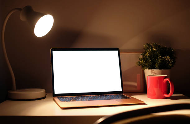 istock Mock up computer laptop with empty display and glowing lamp on wooden table in dark room. 1364128503