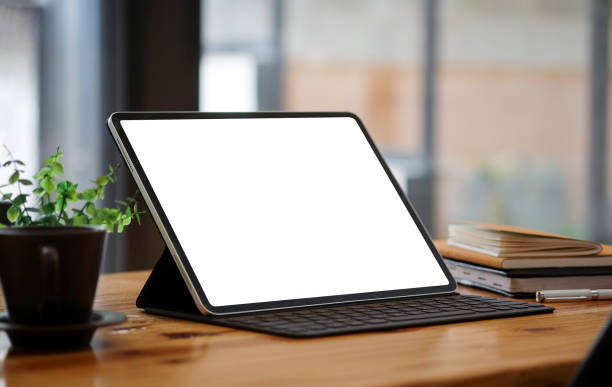 istock Mock up computer tablet with white display, red coffee cup and books on wooden table. 1364128517