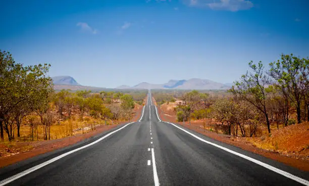 The open road in Kimberly, Western Australia. Straight single lane asphalt road stretching into the distance with mountains in the background. Holiday adventure.