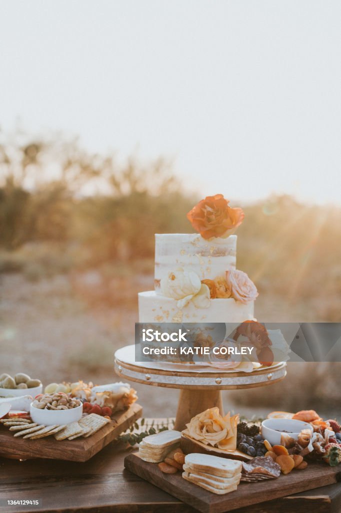 Floral Wedding cake White cream wedding cake with red and pink flowers and food charcuterie near it. Wedding Stock Photo