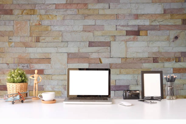 istock Mock up computer laptop, camera, coffee cup and wooden frame on white table with brick wall. 1364130081