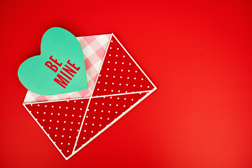 Valentine's Day background with envelope and love heart on a vibrant red background with copy space