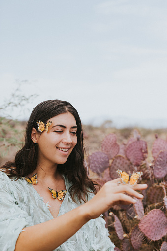 Woman with butterflies landing on her amongst purple prickly pear cactus. Blue fringe fashion top. Shoot for make up company.