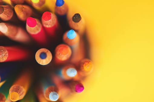 Collection of colored pencils in a jar on a vibrant yellow background with space for copy