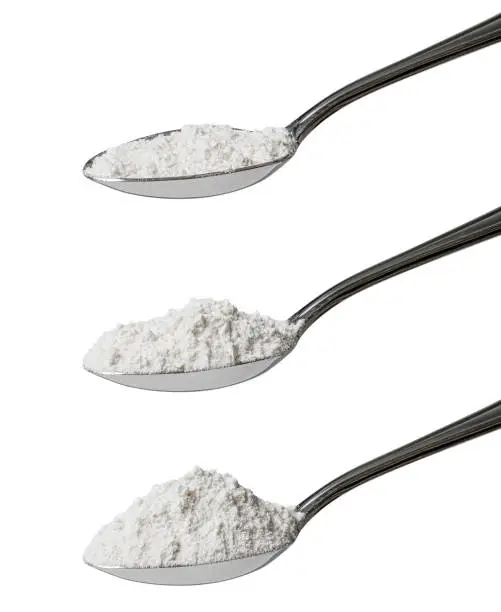 Set of three tablespoons of refined white flour showing an angled view of level, rounded and heaped measurements isolated on a white background