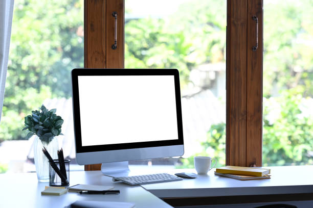 istock Mockup computer with blank screen and office supplies on white table at creative workplace. 1364135365
