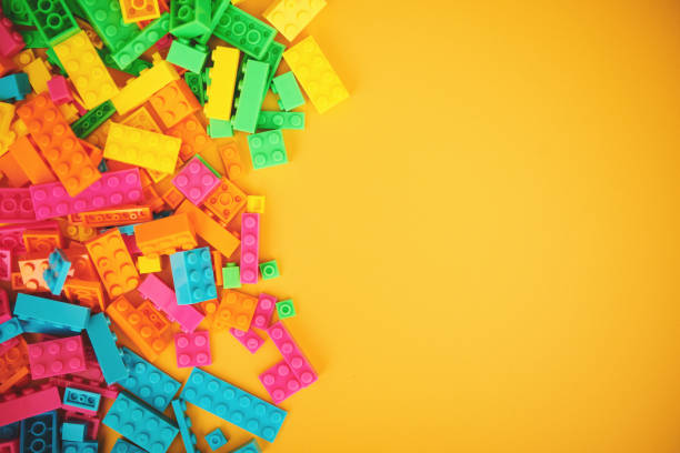 Collection of scattered plastic toy bricks on a bright yellow background with copy space