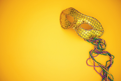 Mardi Gras or carnival background with colorful beads and masquerade mask on vibrant yellow. Overhead shot with copy space