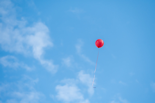 A red balloon flying under the blue sky and white clouds.