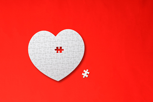 Overhead shot of heart-shaped blank jigsaw puzzle with missing piece on red background.