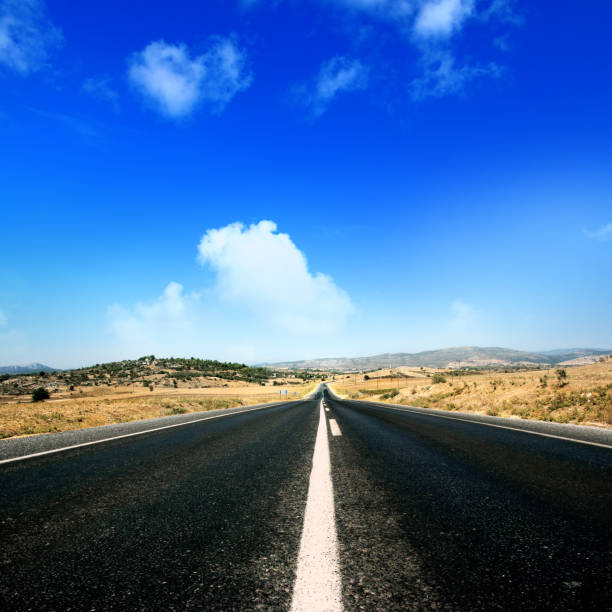istock Empty single lane asphalt road in mountainside landscape over sunny blue sky 1364142742