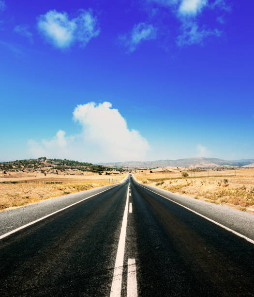 istock Empty single lane asphalt road in mountainside landscape over sunny blue sky 1364142743