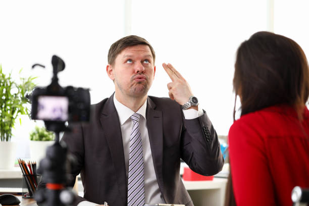 Portrait of businessman giving interview to journalist in office. Man in presentable suit with active expressions. Camera on tripod. Business appointment concept