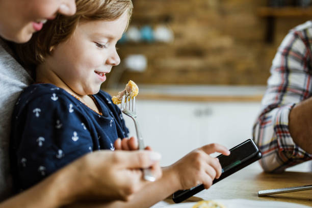 istock Small boy watching cartoons on cell phone during breakfast with his parents. 1364152525