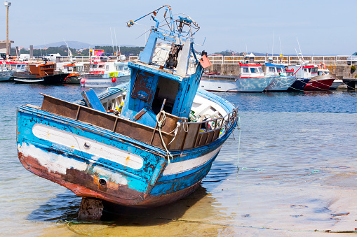 Old fishing boat on harbor dock ,Ribeira, Barbanza, A Coruña province, Galicia, Spain. Rear view, copy space available on the right. Fishing boats in a row moored in the background.