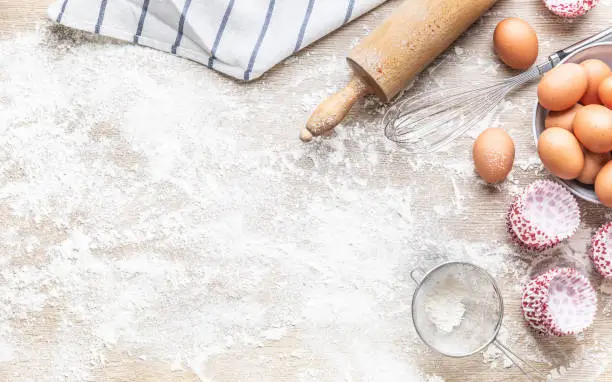 Baking utensils with eggs flour and cupcake cases on kitchen table - Top of view.