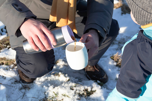 Dad and son in nature in winter drinking hot tea from a mug