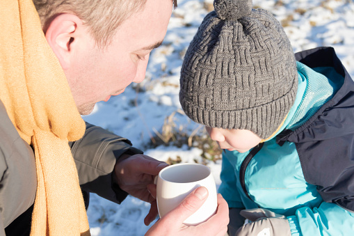 Dad and son in nature in winter drinking hot tea from a mug