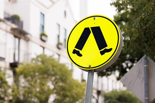 Yellow metal street sign alerting drivers to a pedestrian crossing.