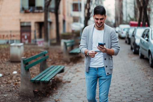 Young  man using mobile phone, shopping online looking at digital screen standing on the street