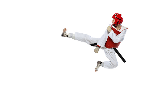 Young girl, taekwondo practitioner training, jumping isolated over white background. Concept of sport, education, skills, workout, health. Sportsman wearing white dobok and protective equipment