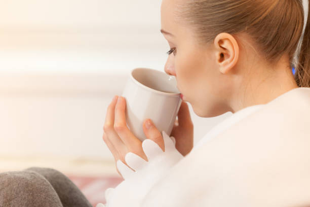 istock Woman lying on sofa under blanket drinking tea 1364172651