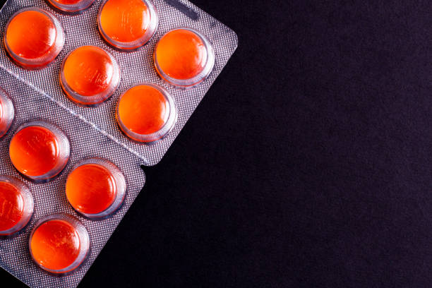 colorful orange tablets on a black background. cough and sore throat. colorful orange tablets in a package on a black background. cough and sore throat. cough lozenge stock pictures, royalty-free photos & images