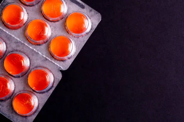 colorful orange tablets in a package on a black background. cough and sore throat.
