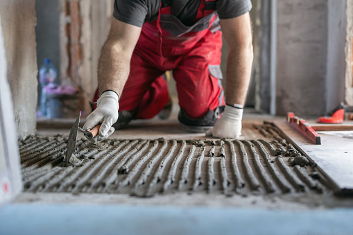 Construction worker spreading and smoothing tile adhesive on the floor
