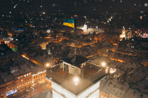 vue aérienne de la vieille ville nocturne de lviv pendant les chutes de neige et le drapeau ukrainien - krakow people poland church photos et images de collection