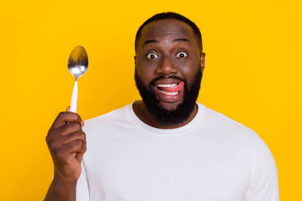 Photo of funny positive handsome guy hold spoon tongue lick teeth lips isolated on yellow color background stock photo