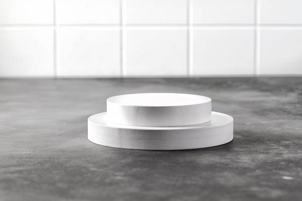 istock Podium. White round podium for presentation. Pedestals on grey background and tile wall. One round podium. 1364187977
