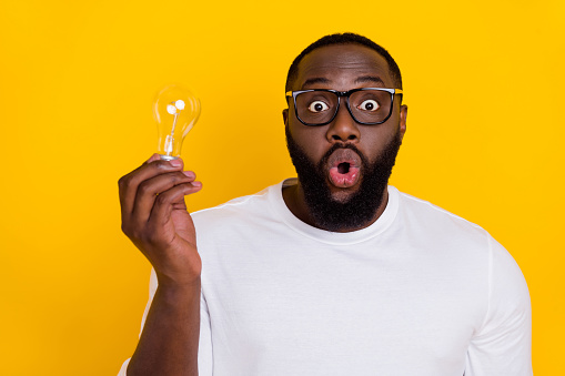Portrait of impressed clever person hold light bulb open mouth look camera isolated on yellow color background.
