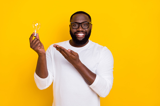 Portrait of candid cheerful person arm hold show light bulb beaming smile isolated on yellow color background