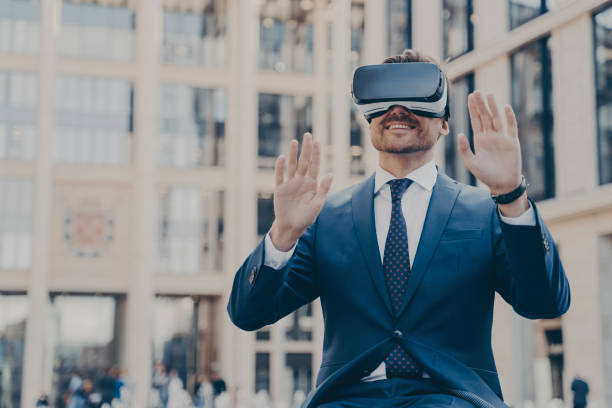 istock Young happy bearded man office worker dressed formally sitting outdoors and using VR headset or 3d goggles 1364190096