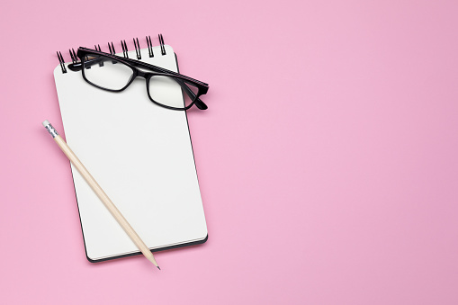 Spiralnotebook glasses and pencil isolated on pink background