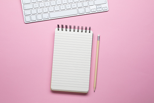 Notebook and computer keyboard isolated on pink background