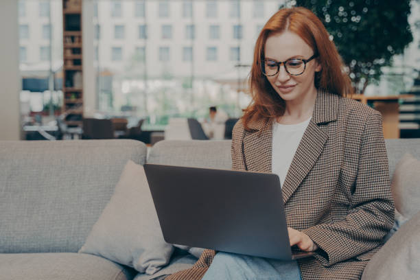istock Woman working remotely in coworking space, using laptop while sitting on couch 1364194355