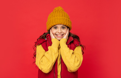 express positive emotion. winter fashion. glad kid with curly hair in hat. female fashion model. teen girl in down vest. portrait of child wearing warm clothes.