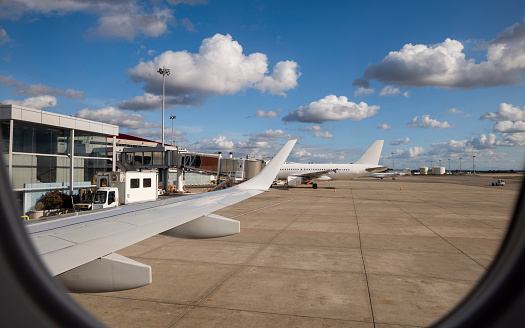 An airplane wing on a plane travelling along a runway at the airport The airport and other stationary planes are in the background.