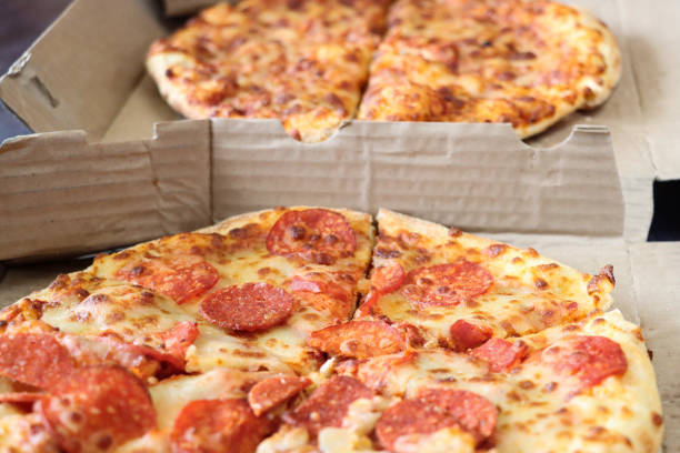 Stock photo showing close-up view of two cardboard takeaway pizza boxes containing sliced pepperoni and margherita pizza, topped with a rich tomato sauce and melted buffalo mozzarella.